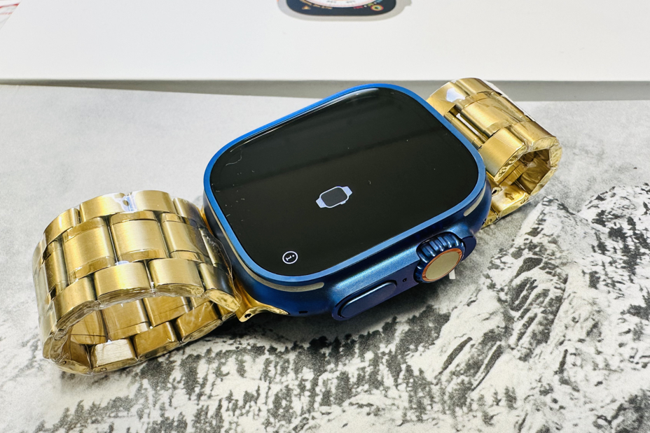 Um Apple Watch Ultra feito sob medida, com caixa azul e pulseira de metal dourado.