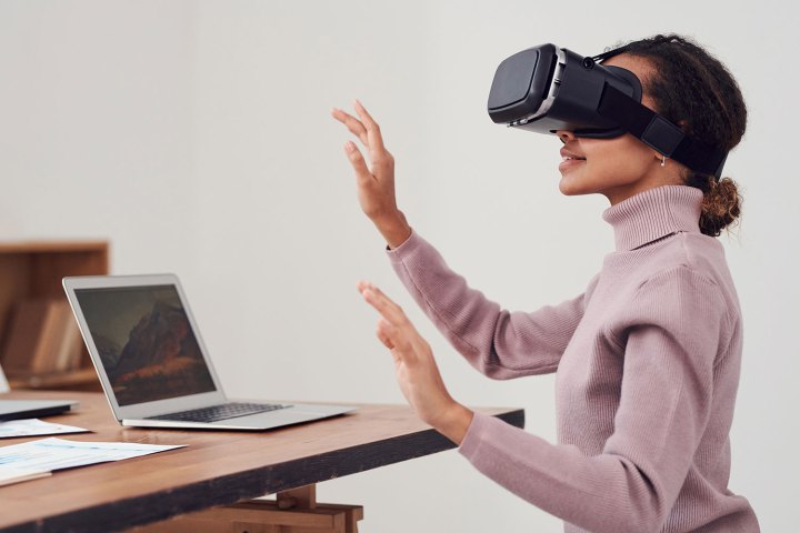 Uma mulher usando um headset VR em uma mesa com um Apple MacBook,