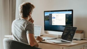 A person sitting at their desk with a desktop computer and two laptops next to them. They are using the 1Password password manager on their computer.