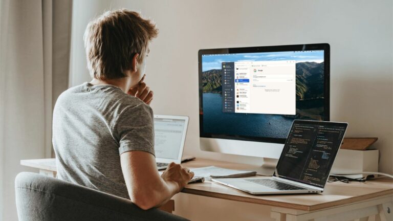 A person sitting at their desk with a desktop computer and two laptops next to them. They are using the 1Password password manager on their computer.