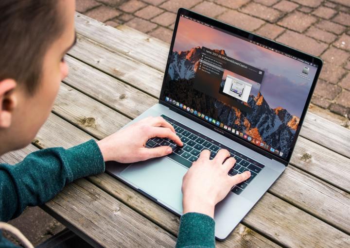 Uma pessoa digitando em um MacBook Pro sentada em um banco de madeira.