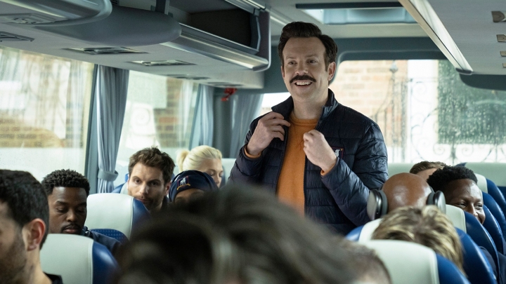 Ted sorrindo em um ônibus na Ted Lasso.