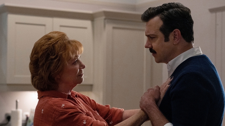 A mãe de Ted, Dottie, com as mãos no peito dele, ele as segurando em uma cena de Ted Lasso.