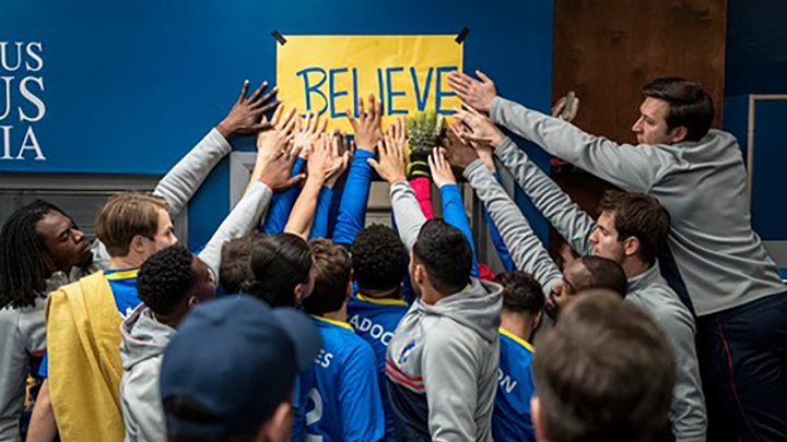 A equipe com as mãos no pôster Believe em uma cena de Ted Lasso.