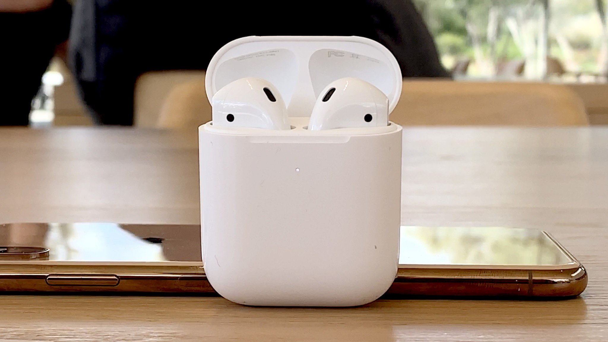 AirPods 2 em um estojo de carregamento contra um iPhone X em uma mesa de madeira