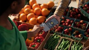 A user in a green top makes a card payment on on an iPhone above a market of fruit