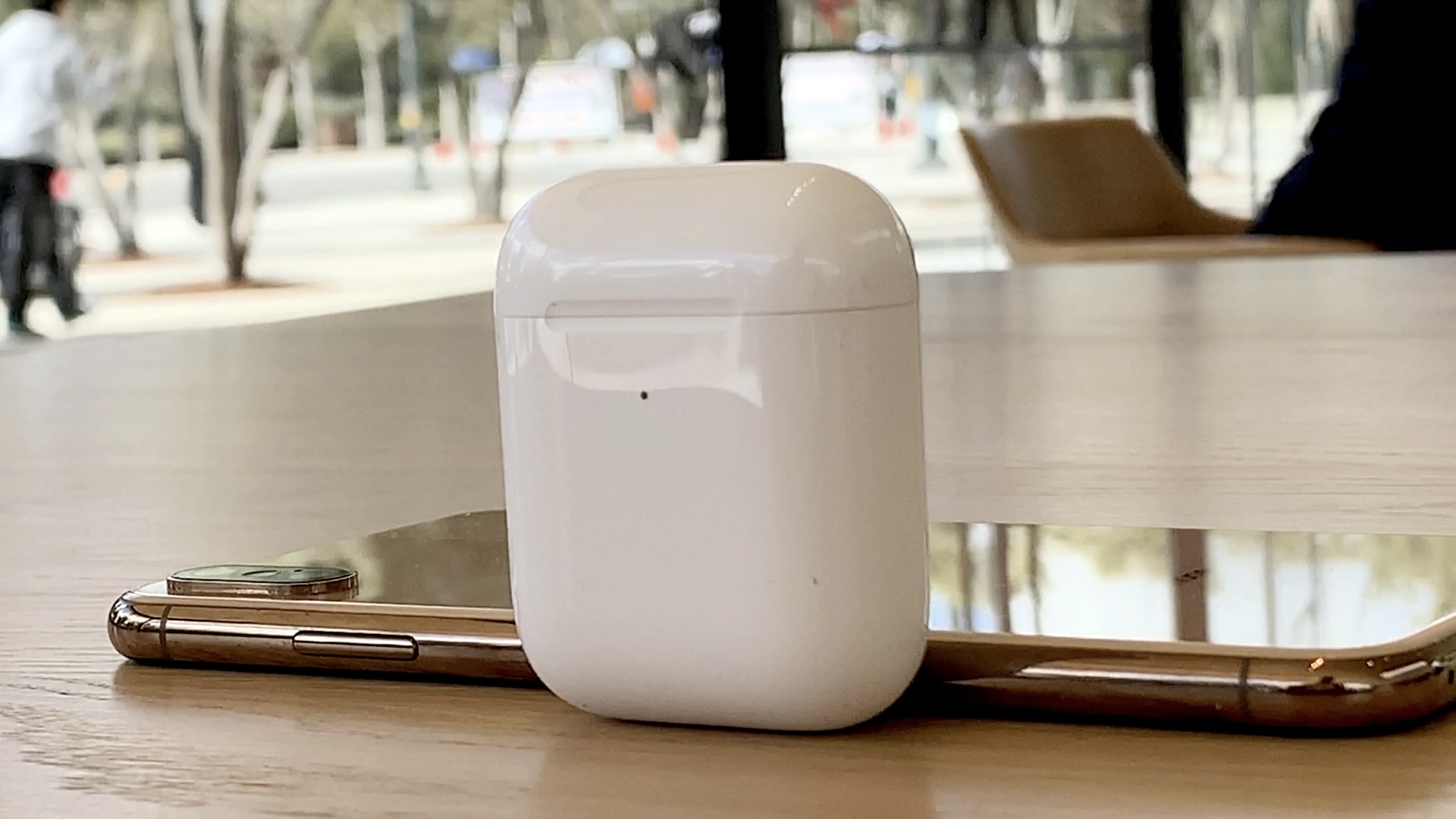 Estojo de carregamento sem fio AirPods 2 em pé sobre a mesa com iPhone XS dourado atrás