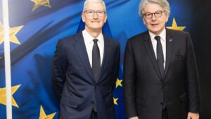 Tim Cook in a suit alongside Thierry Breton, standing infront of the EU flag