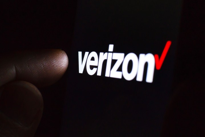 Logotipo da Verizon na tela de um smartphone em um quarto escuro e um dedo tocando nele.