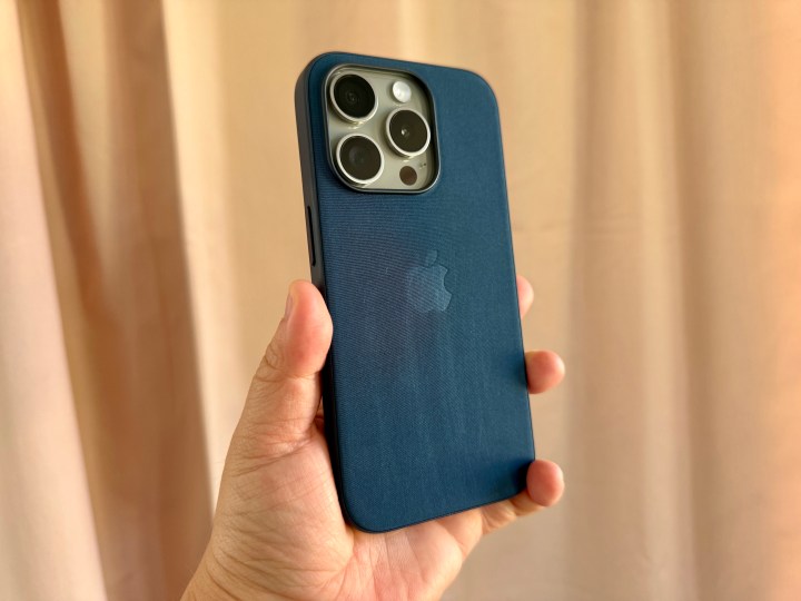 iPhone 15 Pro de titânio natural em capa FineWoven Azul Pacífico, segurado na mão, mostrando desgaste.