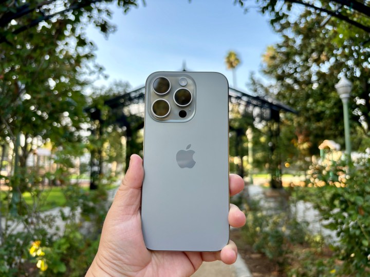 iPhone 15 Pro em titânio natural segurado em um arco de jardim de rosas.