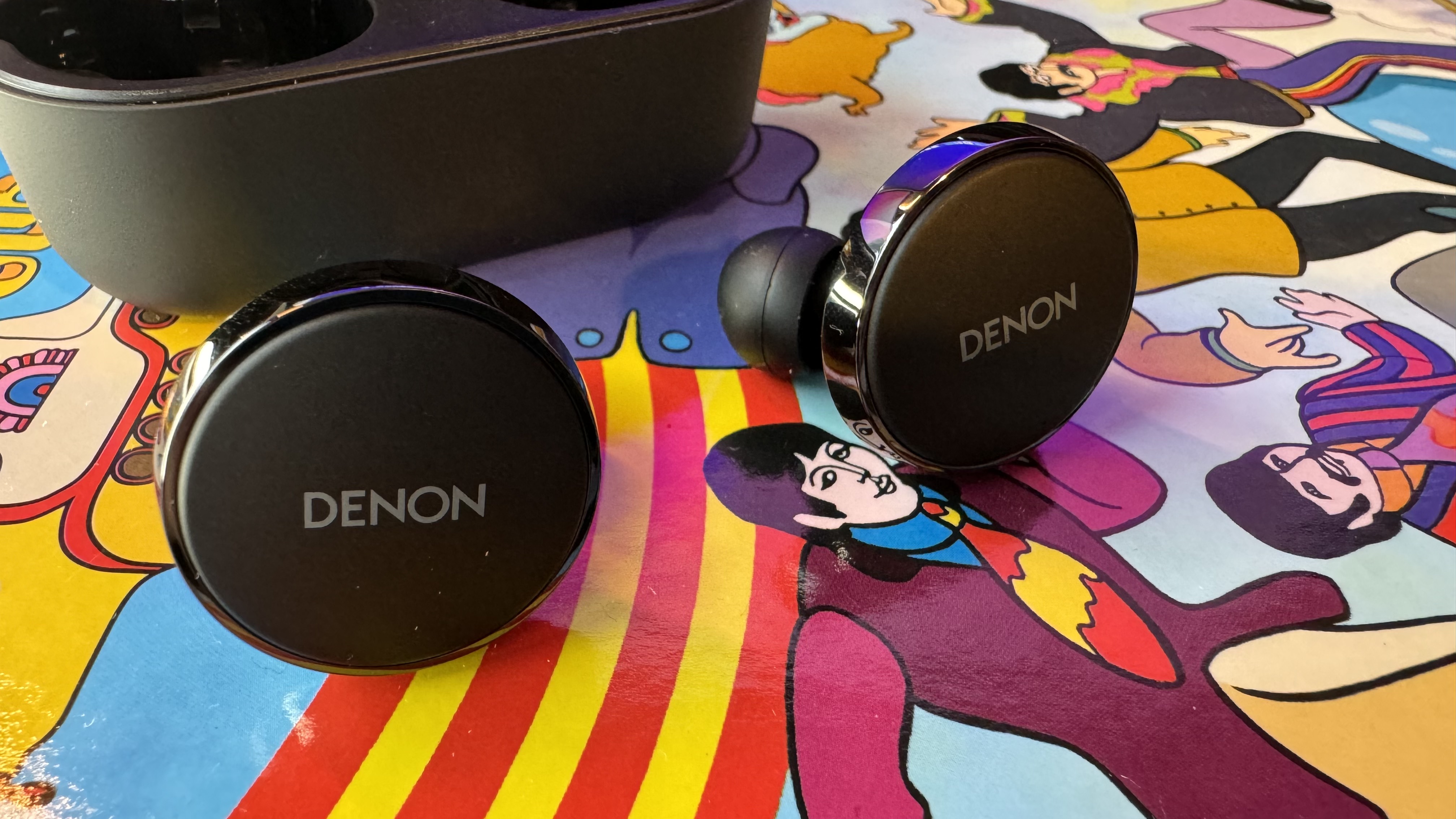 Fones de ouvido Denon PerL Pro em um fundo psicodélico colorido.