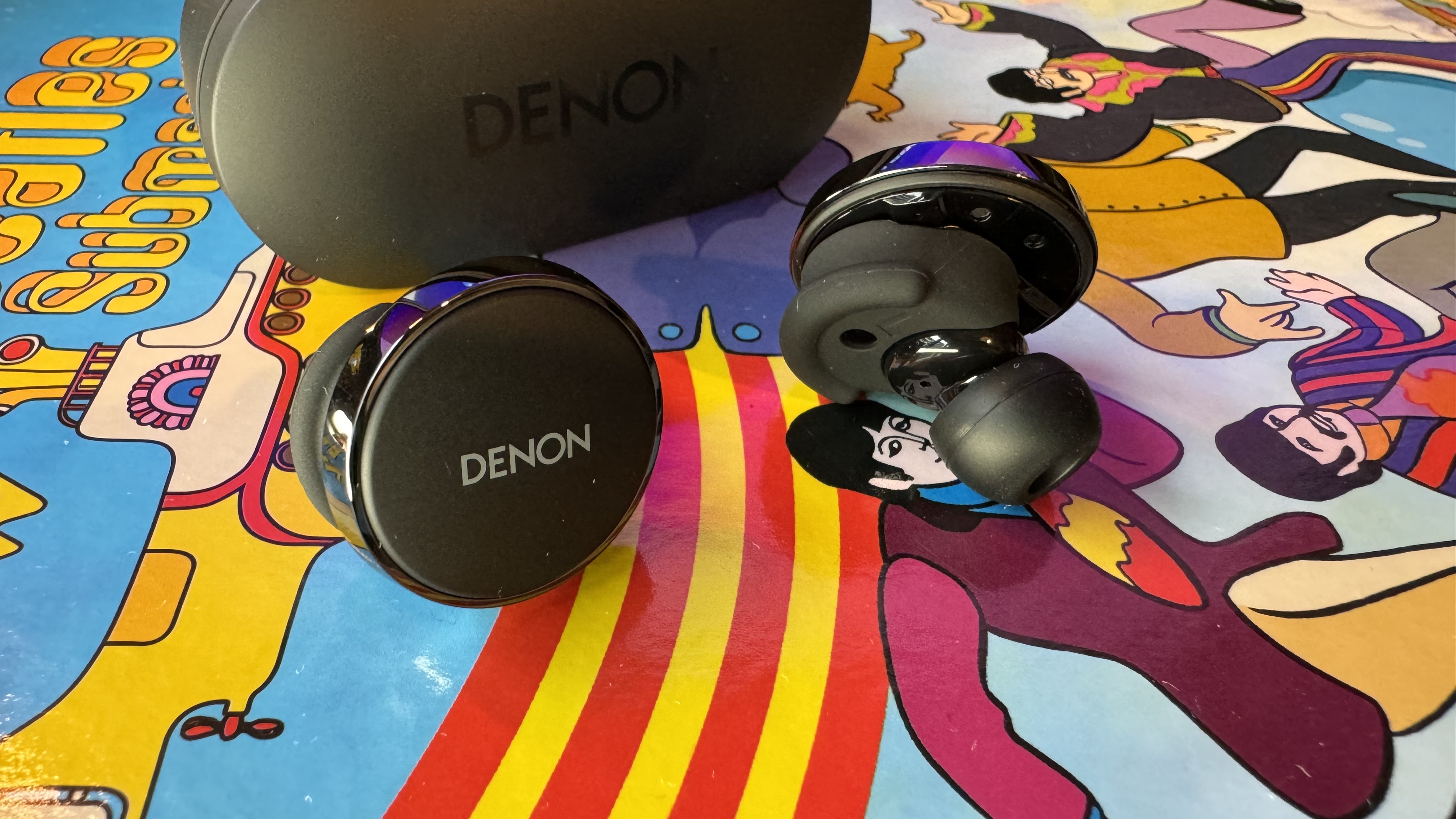 Fones de ouvido Denon PerL Pro em um fundo psicodélico colorido.