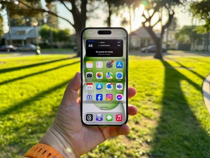 Um iPhone 15 verde na mão mostrando a tela inicial.