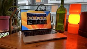 A 2023 14-inch MacBook Pro on a wooden counter, near a retro lamp.