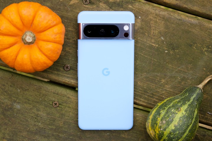 Um Google Pixel 8 Pro azul, virado para baixo ao lado de uma pequena abóbora e uma abóbora.