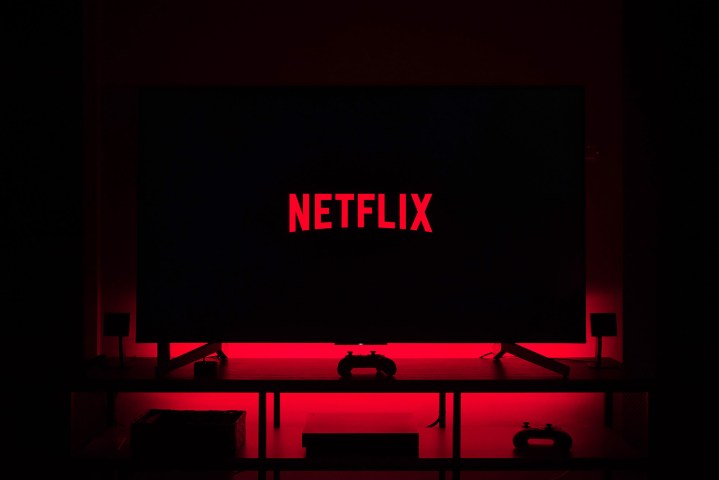 O logotipo da Netflix é exibido na tela da TV enquanto luzes vermelhas iluminam a parede atrás.