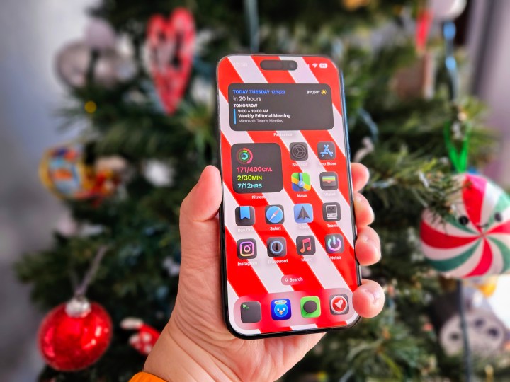 iPhone 15 Pro na mão em frente a uma árvore de Natal.