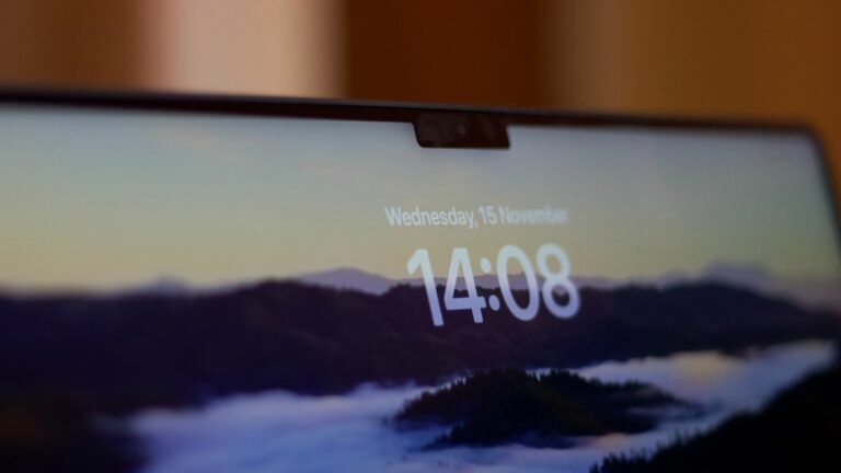 A MacBook display showing the time, 14:08, on a mountain background