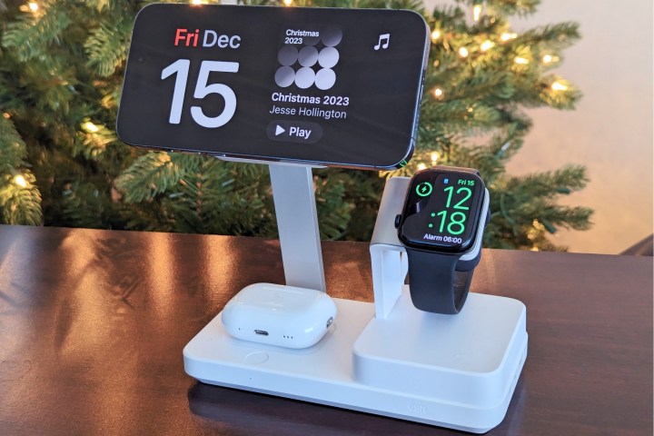 Suporte de carregamento 6 em 1 ESR na mesa em frente a uma árvore de Natal com iPhone 14 Pro Max acoplado no modo StandBy com carregamento do Apple Watch Series 8 e AirPods Pro.