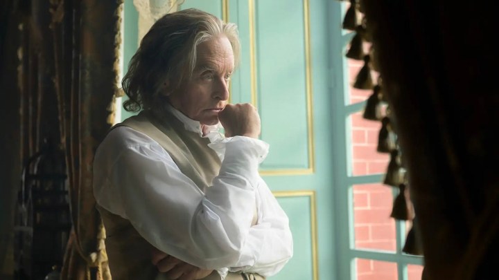 Michael Douglas, como Benjamin Franklin, fica perto de uma janela pensando, com o punho na altura do queixo em uma cena de Franklin.