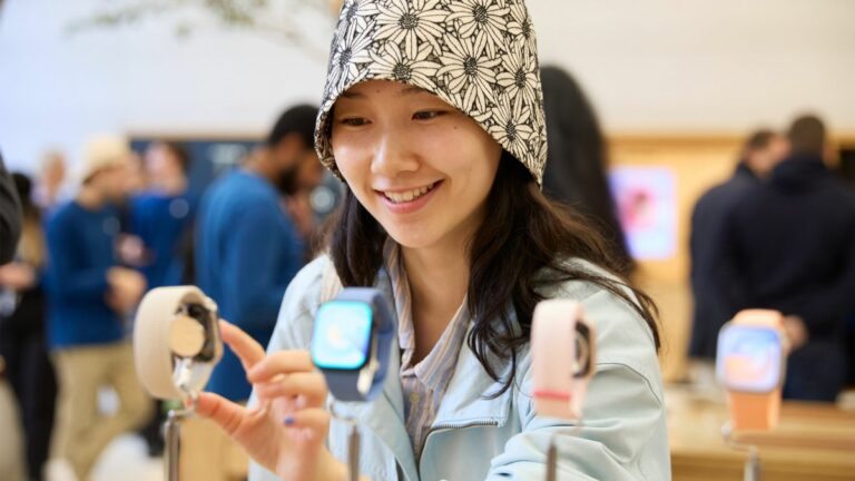 A woman wearing a hat standing in front of an Apple Watch display