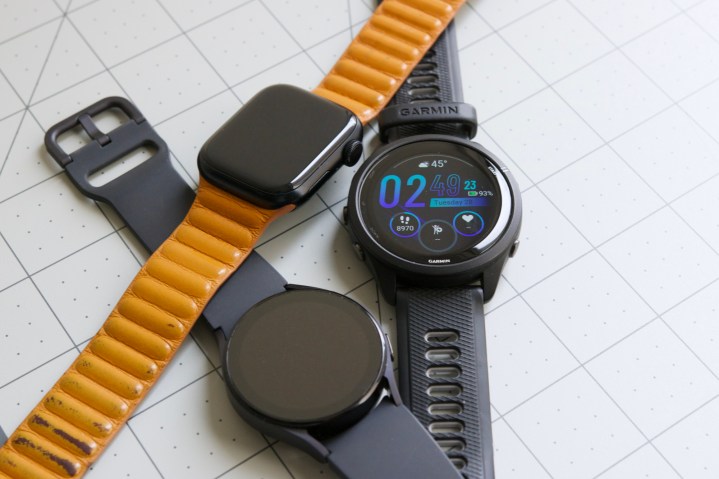 Um Apple Watch, um Galaxy Watch 5 e um Garmin Forerunner 265 sobre uma mesa, um ao lado do outro.