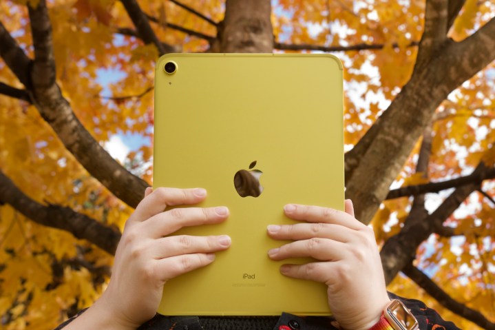 Alguém segurando o iPad amarelo (2022) em frente a árvores com folhas laranja e amarelas.