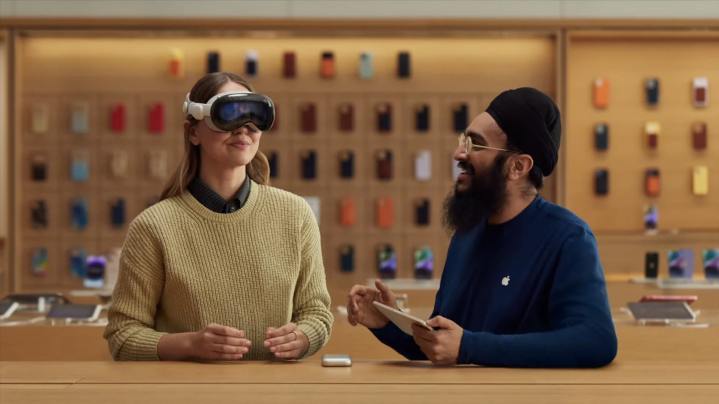 Uma pessoa experimenta um headset de realidade mista Apple Vision Pro em uma Apple Store, com um funcionário da Apple ao lado.