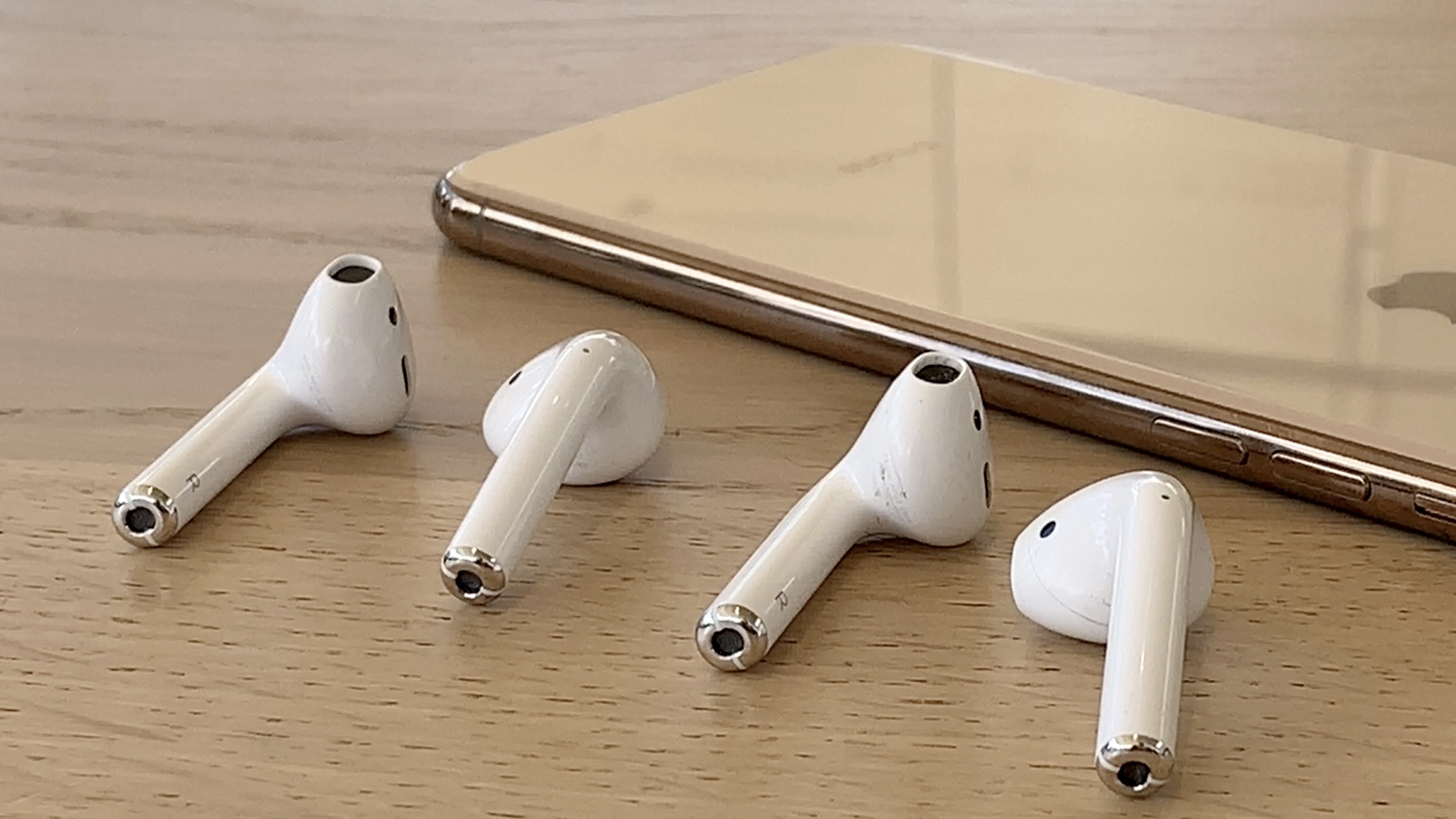 AirPods 2 e AirPods 1 ao lado de um iPhone X em uma mesa de madeira