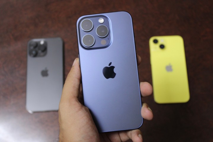 iPhone 15 Pro em mãos com iPhone 14 Pro Max e iPhone 14 em segundo plano.