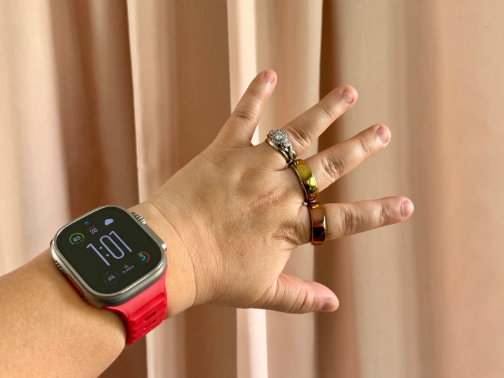 Um Apple Watch Ultra com pulseira vermelha no pulso e Movano Evie e Oura Ring nos dedos.