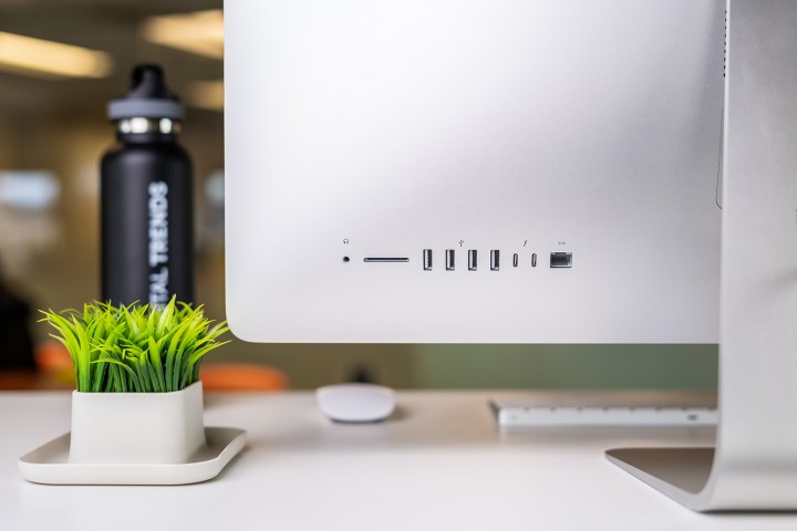 Vista traseira de um iMac sobre uma mesa branca ao lado de um vaso de planta.  Uma visualização na qual você pode ver a seleção de portas do iMac. 