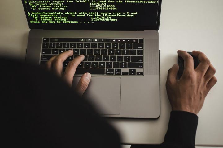 Um hacker digitando em um laptop Apple MacBook, que mostra o código na tela.