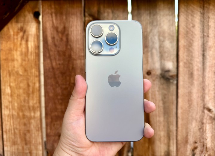 iPhone 15 Pro em titânio natural segurado em frente a um portão de madeira.