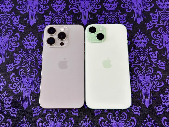Um iPhone 15 Pro de titânio natural (à esquerda) e um iPhone 15 verde em um jogo americano de papel de parede Haunted Mansion.